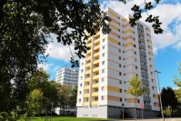 Hochhaus 12 Etagen, Fassade weiß mit gelben Streifen. Davor angelegte Parkplätze, Wiesen mit Bäumen.