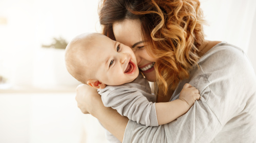 Mutter mit Baby auf dem Arm. Beide lachen.