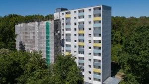 Hochhaus mit 2 Baukörpern, linker Teil mit Baugerüst und Netzen, rechter Teil weiße Fassade mit bunten Balkonbrüstungen. Rundum Bäume. Hochhaus mit 2 Baukörpern, linker Teil mit Baugerüst und Netzen, rechter Teil weiße Fassade mit bunten Balkonbrüstungen. Rundum Bäume.