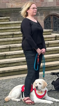 Frau mit Asistenzhund mit rotem Leibchen