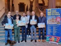 Mehrere Personen und ein Hund stehen vor einer Treppe, einige davon halten ein bunt bemaltes Papier in den Händen