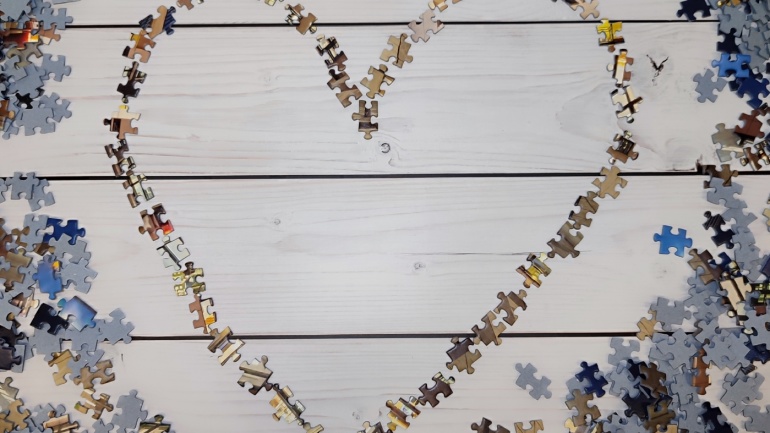 Das Bild zeigt einen Dielenboden aus hellem Holz, auf dem ein Herz aus zufälligen Puzzleteilen liegt, die lose zu einen Herz zusammengelegt wurden. Um dieses Herz liegt in einem Abstand ein Kranz aus weiteren Puzzleteilen. Das Bild zeigt einen Dielenboden aus hellem Holz, auf dem ein Herz aus zufälligen Puzzleteilen liegt, die lose zu einen Herz zusammengelegt wurden. Um dieses Herz liegt in einem Abstand ein Kranz aus weiteren Puzzleteilen.