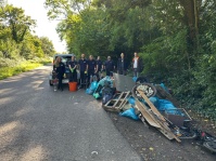 Mehrere Menschen stehen an einer Straße am Waldrand vor eine Anhänger mit vielen Mülltüten und eingesammeltem Sperrmüll