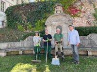 Menschen in Gärtnerbekleidung mit Spaten vor einen historischen Brunnen