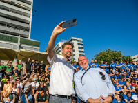 Zwei Männer machen ein Selfie, im Hintergrund sitzen viele Menschen auf einer Treppe