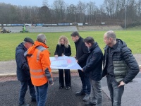 Sechs Personen stehen neben einer Sportanlage und begutachten einen Bauplan