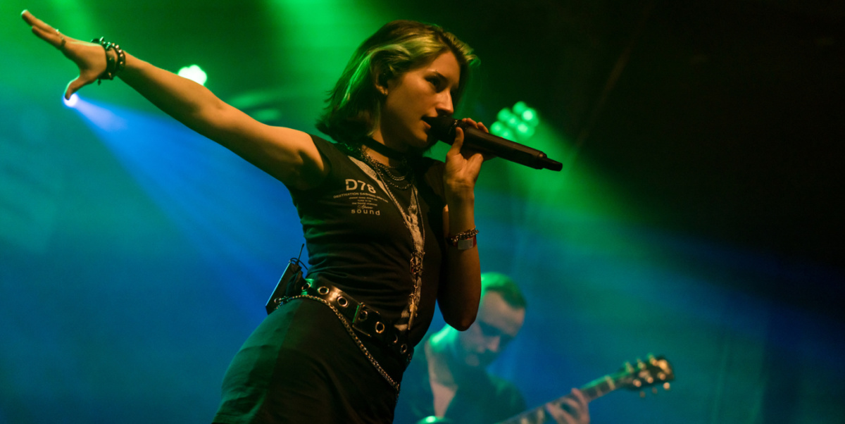 Rocksängerin streckt Arm aus, Gitarrist im Hintergrund