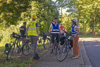 Eine Gruppe von Menschen mit Fahrrädern pausieren ihre Radtour an einem begrünten Ort.