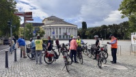 Eine Gruppe von Menschen mit Fahrrädern pausieren ihre Radtour auf dem Tbilisser Platz vor dem Saarländischen Staatstheater.