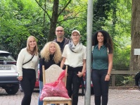 Fünf Personen stehen bei einer Müllsammelaktion neben einem Stuhl, auf dem ein gefüllter roter Müllsack liegt.