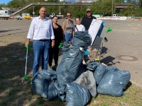 Fünf Personen stehen bei einer Müllsammelaktion hinter mehreren gefüllten Müllsäcken und einem Einkaufswagen.