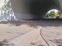 Graffiti an einer Betonwand unter einer Brücke, daneben ein Halteverbotsschild und eine bewachsene Treppe.