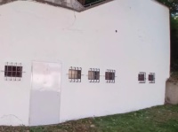 Frisch gestrichene Außenwand eines Gebäudes mit vergitterten Fenstern und einer Tür, davor eine Rasenfläche.