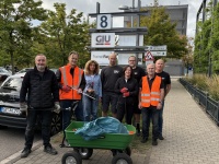Acht Personen stehen mit Müllgreifern und Handschuhen vor dem GIU-Verwaltungsgebäude. Vor ihnen steht ein grüner Handwagen.
