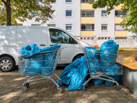 Zwei Einkaufswagen sind mit blauen Müllsäcken gefüllt. Weitere volle Müllsäcke liegen daneben.
