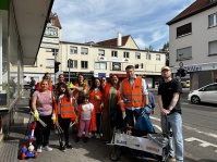 Erwachsene und Kinder mit Warnwesten, Müllgreifern und Sammelwagen bei einer Aufräumaktion in Burbach.