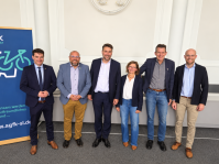 Sechs Personen stehen nebeneinander und lächeln in die Kamera. Links steht ein Aufsteller der AGFK-SL.