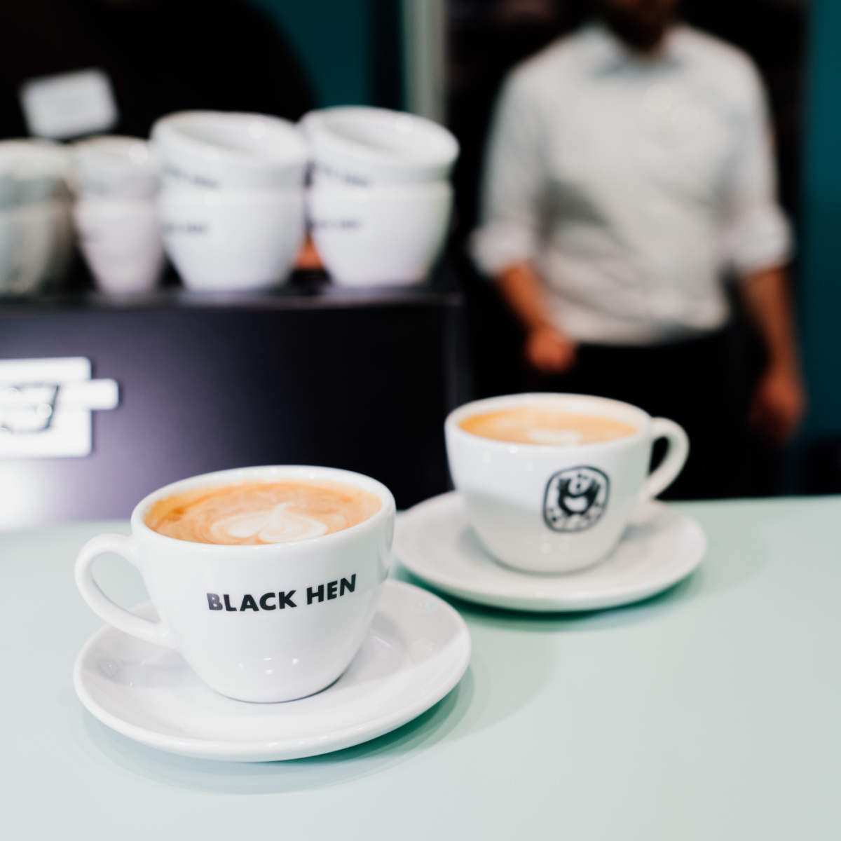 Kaffeespezialitäten bei der Expo Real Zwei volle Kaffeetassen der Marke Black Hen stehen auf dem Tresen.